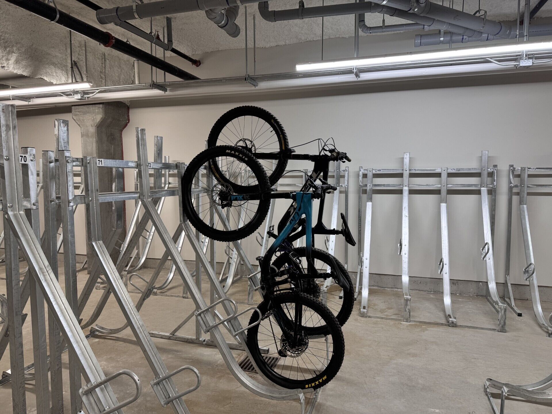 A bicycle rack with multiple bikes, a concrete floor, and industrial-style ceiling pipes.