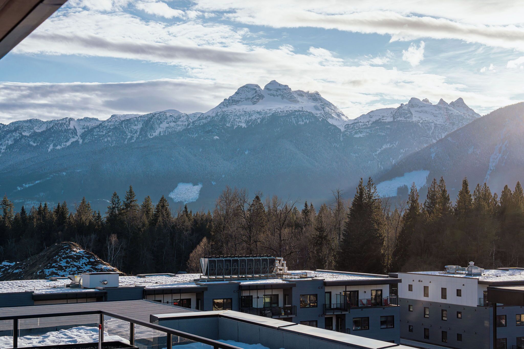 Un hôtel moderne offrant une vue sur des montagnes enneigées et une vallée boisée.