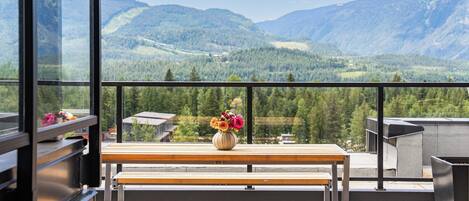 Un balcón con banco de madera y un jarrón de flores, con vistas a un paisaje montañoso.
