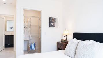 A hotel room with a bed, a nightstand with a lamp, a framed picture on the wall, and a walk-in closet with hanging clothes.