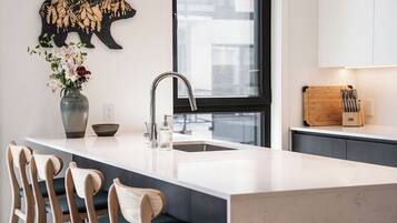 A modern kitchen with a large island, bar stools, a vase with flowers, a bear wall decoration, and a window.