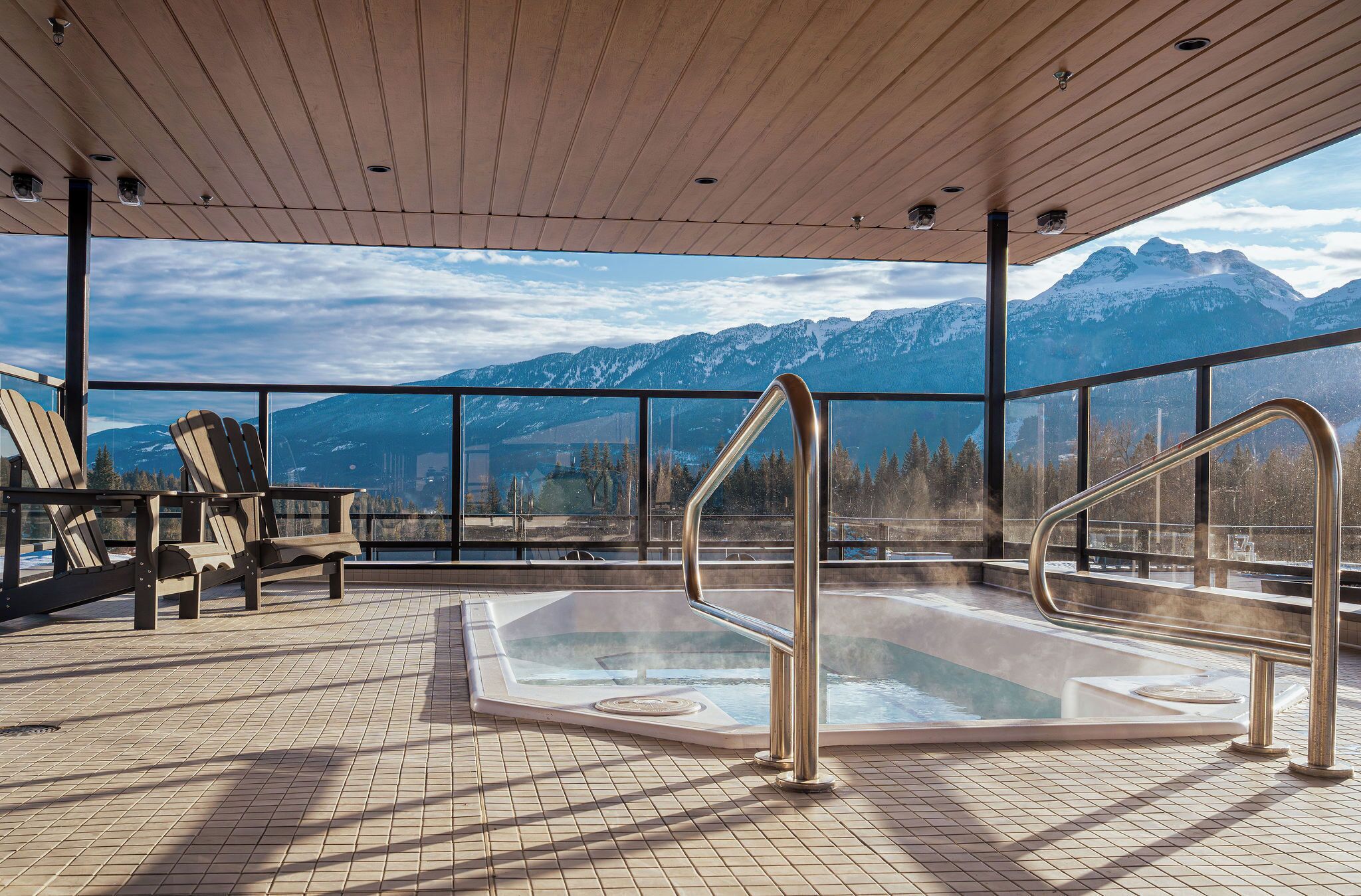 Un bain à remous avec vue sur les montagnes, une terrasse en bois et des fauteuils Adirondack.