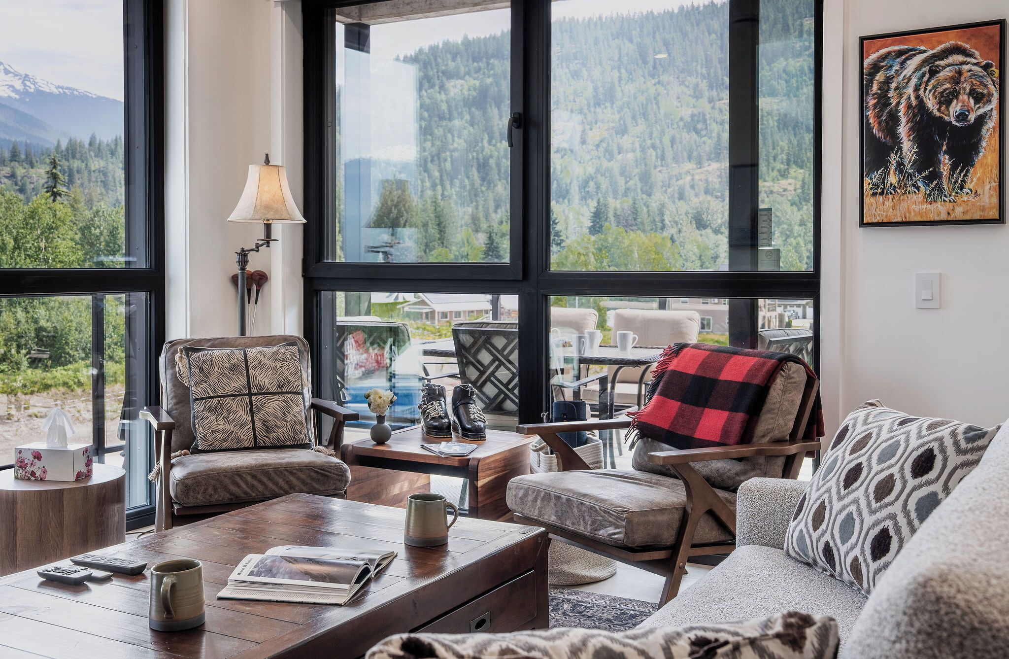 A cozy living room with large windows, a fireplace, and a view of a forested mountain range.