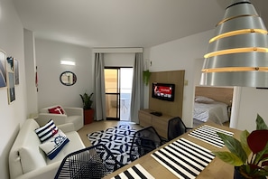 Quarto de hotel moderno com sofá, mesa de jantar, televisão e cama.