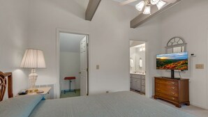 Ein Schlafzimmer mit einem Bett, einer Kommode, einem Fernseher und einer Tür zu einem weiteren Raum.
