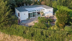 A modern house with a large glass door, surrounded by dense greenery. - Dune Villa with a View | Greenhouse, Piano, and Beach Nearby (Ouddorp)