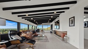 A modern living room with leather furniture, a fireplace, and large windows offering a view of the desert. - S Haus: Elevated Desert Retreat Breathtaking Views (Phoenix)