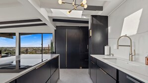 A modern kitchen with a large island, dark cabinetry, and a view through a glass door. - S Haus: Elevated Desert Retreat Breathtaking Views (Phoenix)