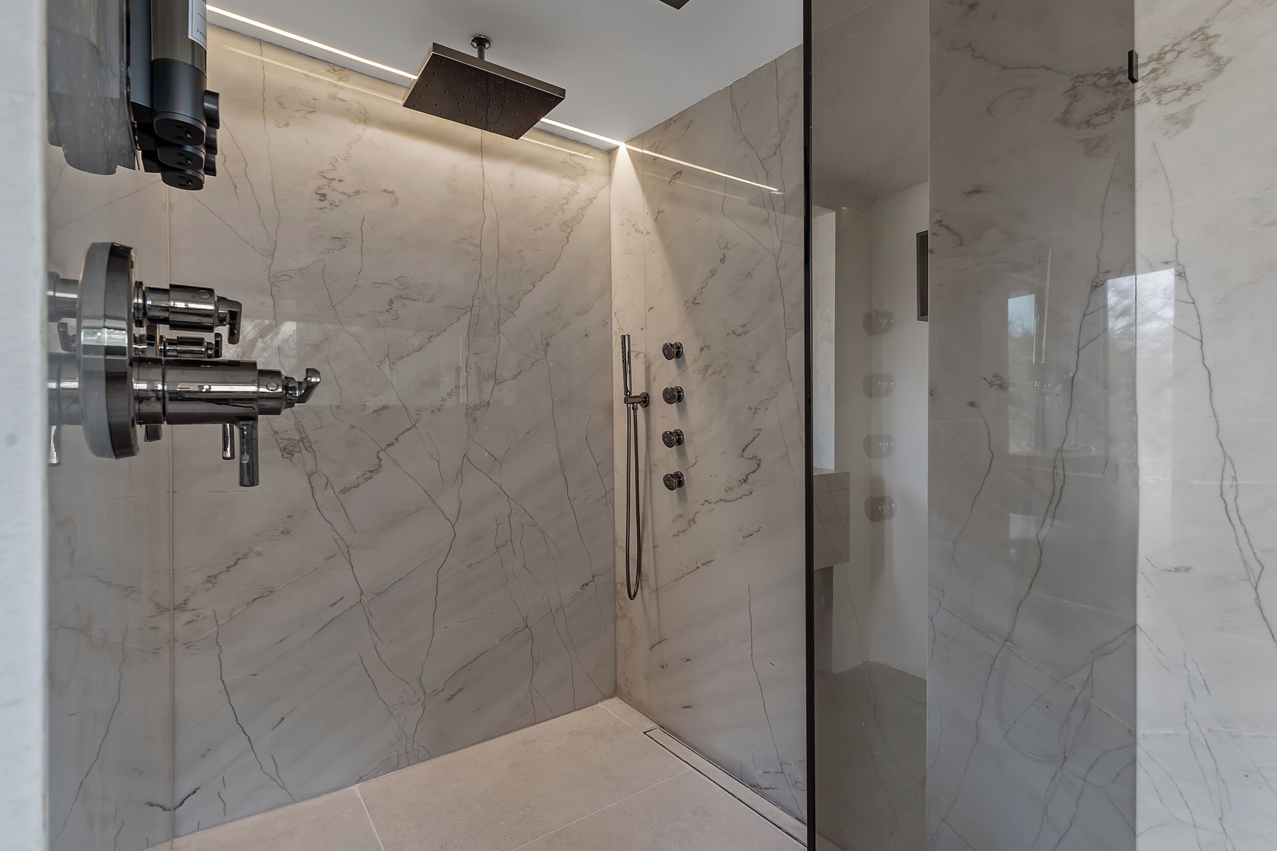 A modern shower with a glass enclosure, marble walls, and a sleek faucet.