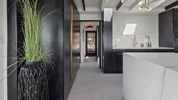 A modern kitchen with a marble countertop, a black vase with green plants, and a skylight above. - S Haus: Elevated Desert Retreat Breathtaking Views (Phoenix)