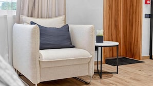 A modern room with a beige sofa, a small round table, and a wooden panel wall. - Marmi Boutique Hotel Jurmala (Jūrmala)