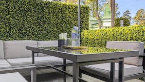 An outdoor seating area with a glass-top table, cushioned sofas, and a neatly trimmed hedge in the background. - Marmi Boutique Hotel Jurmala (Jūrmala)