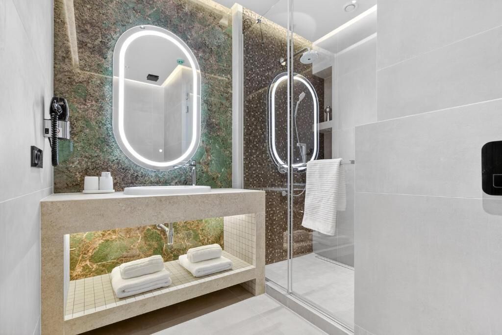 Ein modernes Badezimmer mit einer in Glas eingefassten Dusche, einem мрамор-verkleideten Waschtisch und einem großen Spiegel mit integrierter Beleuchtung.