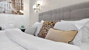 A neatly made bed with white linens and patterned pillows, a grey upholstered headboard, and a wall-mounted light fixture. - Marmi Boutique Hotel Jurmala (Jūrmala)
