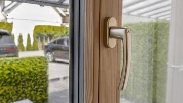 Puerta con manija moderna, ventana de vidrio y vista a un estacionamiento con coches y vegetación.