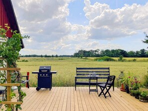 Eine Holzterrasse mit Grill, Bank und Blumentöpfen.