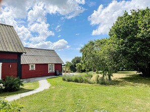 A red building with a metal roof, a paved pathway, and a grassy area with trees. - 4 Star Holiday Home in Visby (Visby)