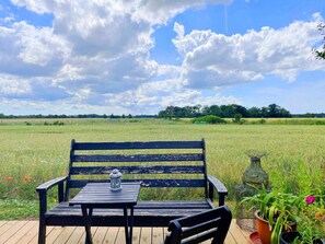 Eine hölzerne Bank mit einem Metalltisch und einer Laterne auf einem Holzdeck mit Blick auf ein Feld.