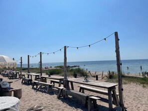 Eine Strandlage mit Holztischen und -bänken, Lichterketten und einem überdachten Bereich.