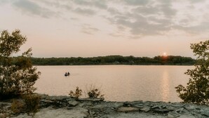 Un lago tranquilo al atardecer con un barco a lo lejos y árboles en la orilla.
