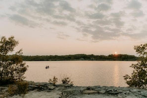 A calm lake at sunset with a boat in the distance and trees on the shore. - Cress Tent | Canvas Tent with Lake Access (Kirkfield)