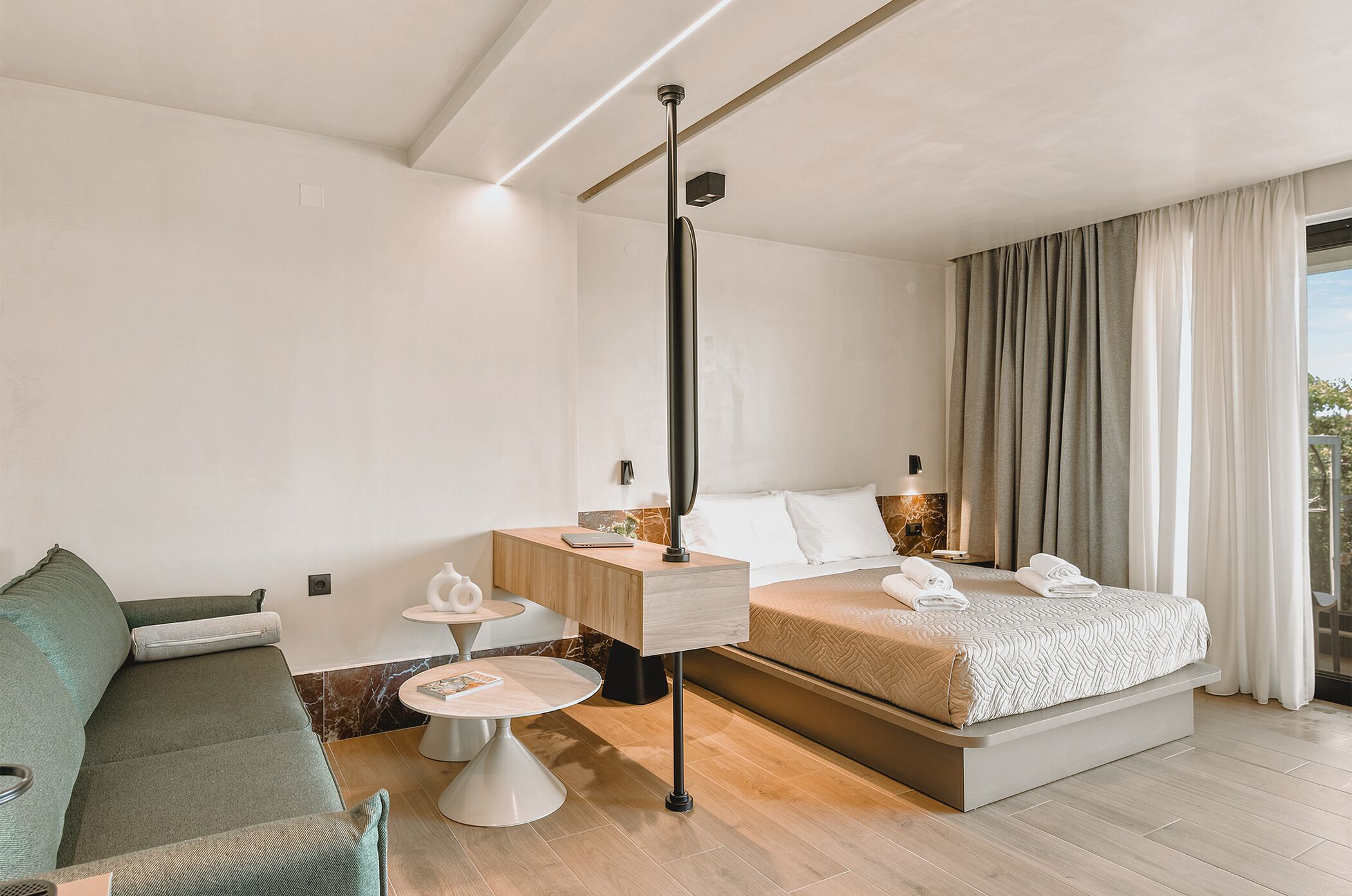 Una habitación de hotel moderna con una cama, un sofá, una mesita y una lámpara.