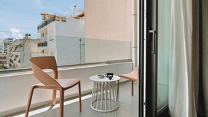 Ein Balkon mit zwei Stühlen und einem kleinen runden Tisch, einer Glastür und Blick auf Gebäude im Hintergrund.