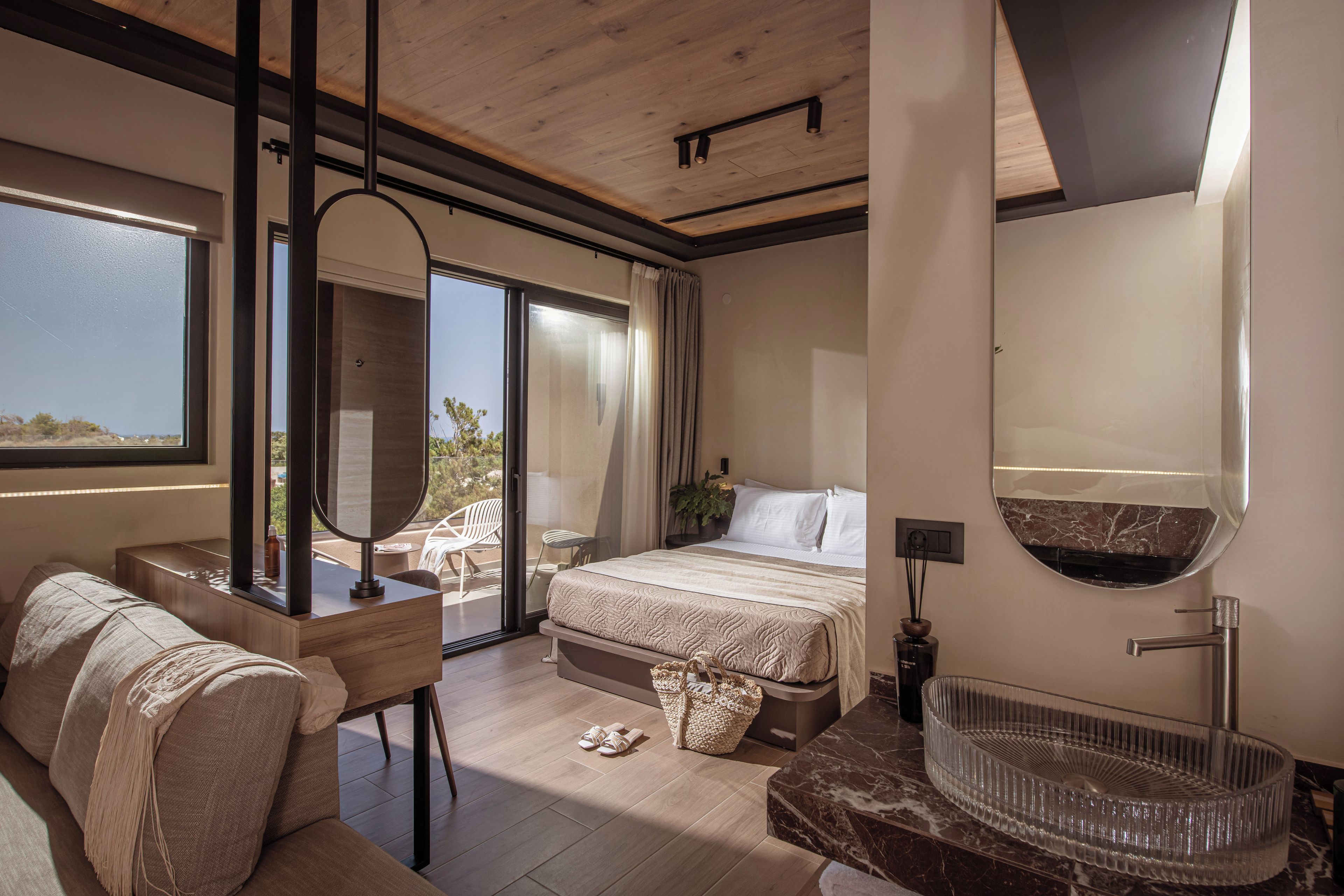 Ein modernes Schlafzimmer mit einem Bett, einer Sitzecke mit einer Couch, einem Schreibtisch und einem großen Fenster.