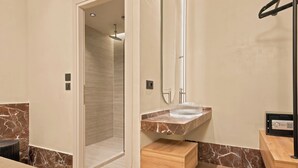 A bathroom with a shower, a marble countertop, a wooden drawer, and a black object on the counter. - MAHA Her City Living by Semavi (Heraklion)