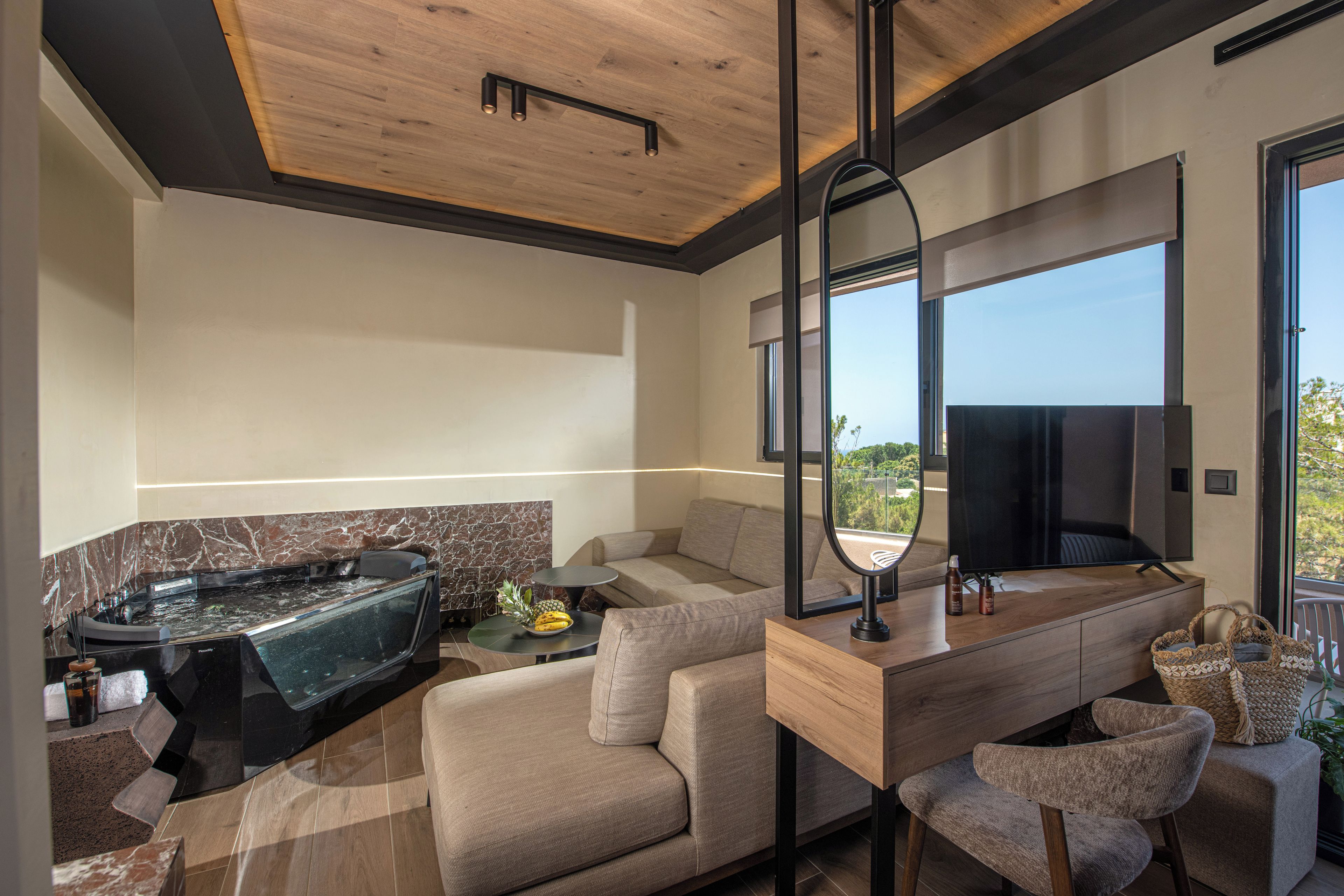 A modern living room with a sofa, a coffee table, a TV, and a large window offering a view of the outdoors.