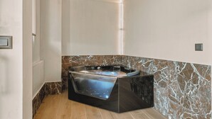 Un baño moderno con una bañera independiente, paredes de mármol y suelo de madera.