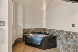 A modern bathroom with a freestanding bathtub, marble walls, and a wooden floor. - MAHA Her City Living by Semavi (Heraklion)
