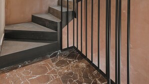 Una escalera con una lámpara circular, barandillas de metal y piso de mármol.