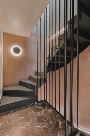 A staircase with a circular light fixture, metal railings, and a marble floor. - MAHA Her City Living by Semavi (Heraklion)