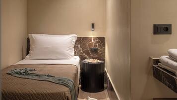 A hotel room with a bed, a nightstand, a marble wall, a towel rack, and a power outlet.