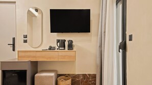 A hotel room with a flat-screen TV, a minibar, a coffee maker, a small refrigerator, a cushioned bench, and a woven basket. - MAHA Her City Living by Semavi (Heraklion)