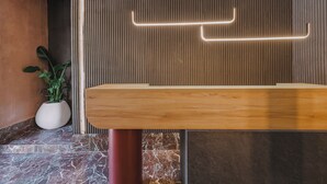 Un mostrador de recepción con detalles de madera, una planta en maceta y una pared con líneas verticales y luz de neón.