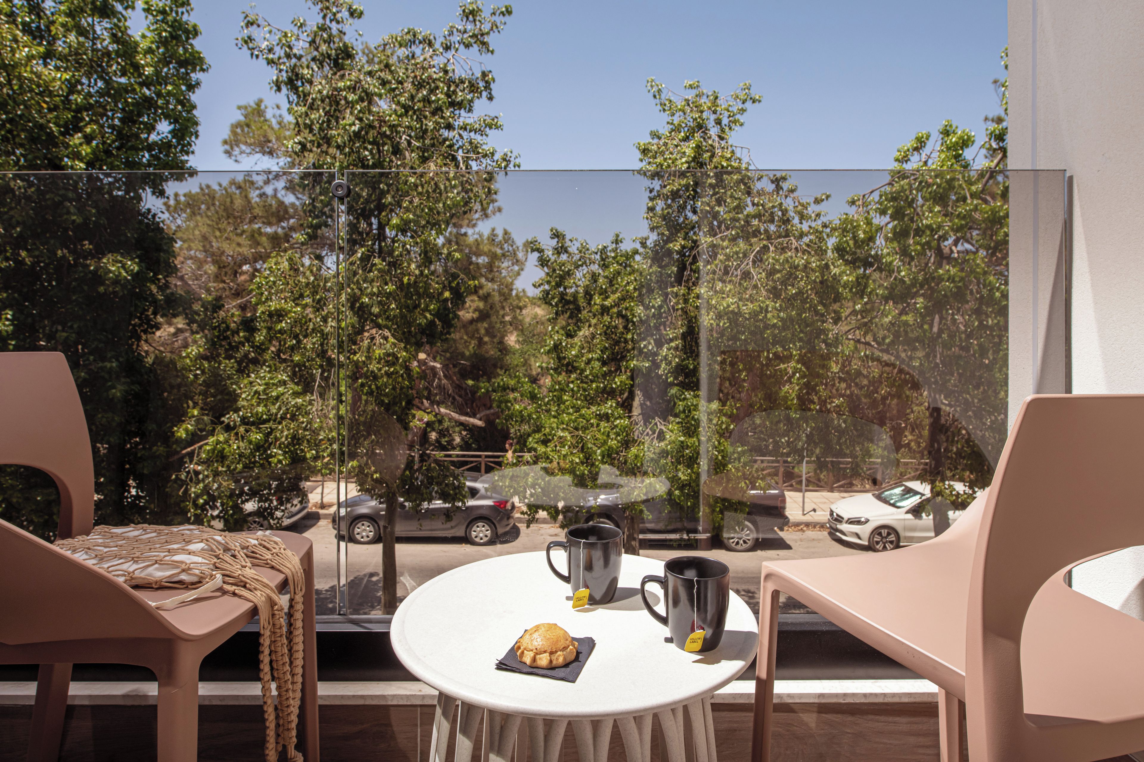 A balcony with a table, chairs, and a view of parked cars and trees.