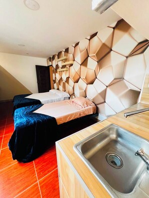 Habitación de hotel con diseño moderno, destacando un cabecero con patrón hexagonal, una mesa de comedor de madera con lavamanos y un piso con baldosas rojas.