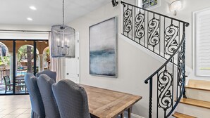 Ein Essbereich mit Holztisch und Stühlen, einer Hängeleuchte, einer Treppe mit aufwendiger Geländer und einem großen abstrakten Gemälde an der Wand.