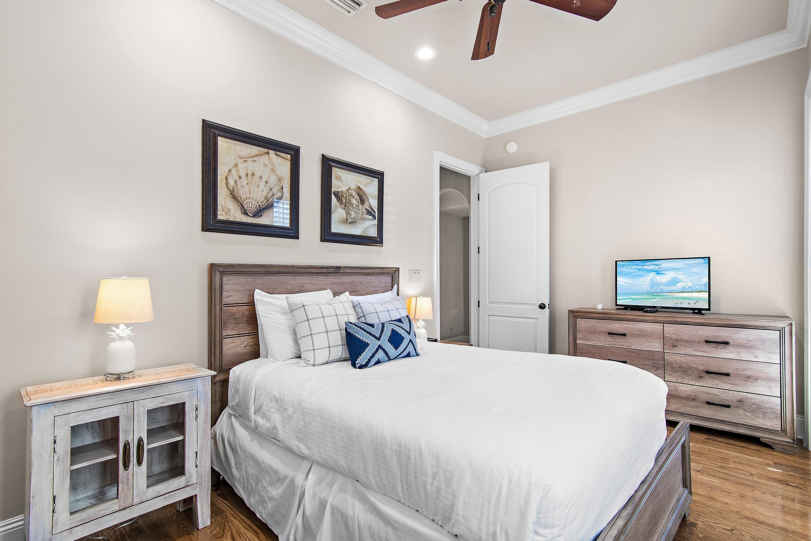 A bedroom with a bed, nightstands, a dresser, a television, and framed pictures on the wall.