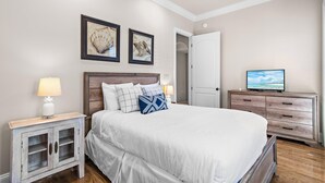 Ein Schlafzimmer mit einem Bett, Nachttischen, einer Kommode, einem Fernseher und gerahmten Bildern an der Wand.