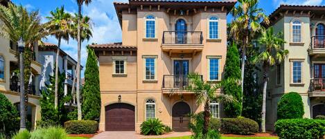 A multi-story building with a central entrance, balconies, and surrounding greenery.