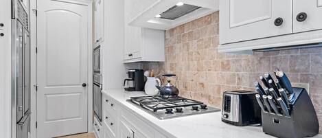 A kitchen with white cabinets, a gas stove, a toaster, and a knife block.