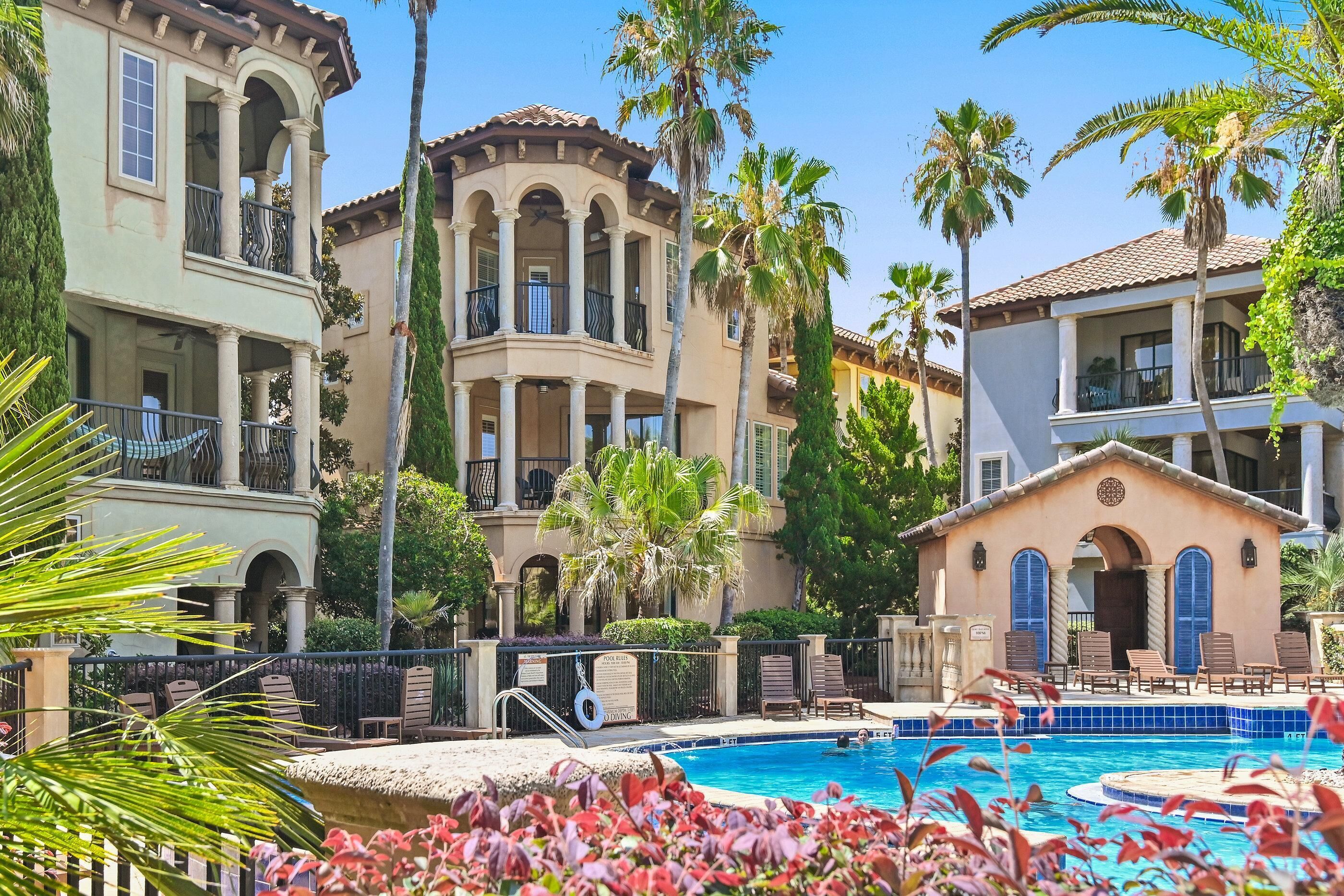 A resort with a swimming pool, palm trees, and Mediterranean-style architecture.