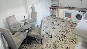 A compact kitchen with a dining area, a washing machine, and a small refrigerator.