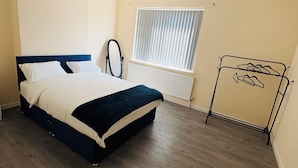 A bedroom with a bed, a radiator, a window with blinds, and a coat rack.