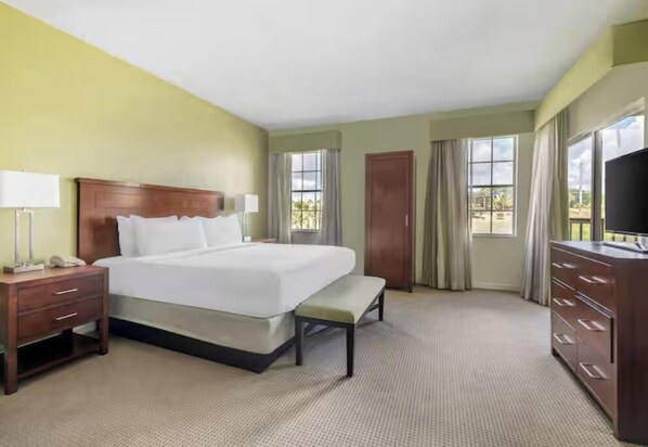 A hotel room with a large bed, bedside tables, a bench, a dresser, and a TV. - Your Ideal Home Base for Every Adventure! Outdoor Pool, with Full Kitchen! (Celebration)