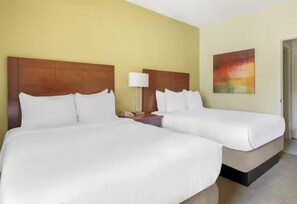 A hotel room with two beds, a nightstand with a lamp, and a painting on the wall. - Your Ideal Home Base for Every Adventure! Outdoor Pool, with Full Kitchen! (Celebration)
