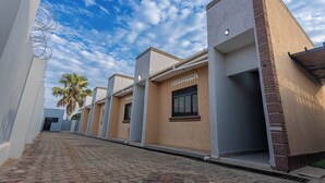 Uma fileira de edifícios modernos com um passeio pavimentado, uma palmeira e céu claro.